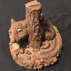 May include: A brown ceramic figurine of a squirrel sitting next to a tree stump with a beetle on the tree. The squirrel is surrounded by acorns and leaves. The base of the figurine is inscribed with "Nell 63".