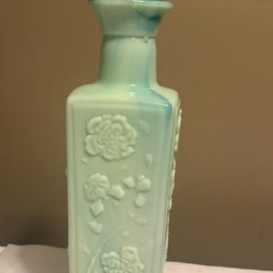 May include: A vintage glass bottle with a swirl of blue and white glass. The bottle has a square shape and is decorated with raised floral designs. The bottle has a matching lid with a pointed top.