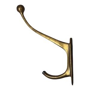 May include: A wall-mounted brass coat hook featuring a long, curved upper arm ending in a rounded ball tip and a shorter, smaller lower hook. The metal has a polished gold-toned finish with visible surface texture and two mounting holes.