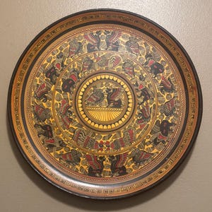 May include: Round decorative tray with a black rim and a gold and yellow center. The tray features a repeating pattern of mythical creatures in red, black, and gold, with a Greek key border.