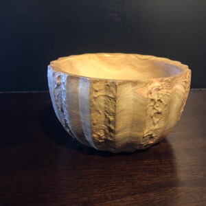 May include: A handcrafted, textured bowl with a light brown and beige marbled appearance. The bowl has a unique, ridged exterior and a smooth interior. The bowl is likely made of ceramic or stone and is suitable for decorative or functional use.