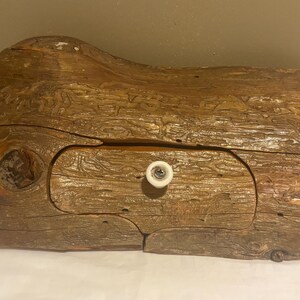 May include: A rustic wooden box with a drawer. The box is made from a piece of wood, with a natural grain and texture. The drawer has a white knob. The box is approximately 12 inches long, 6 inches wide, and 4 inches tall.