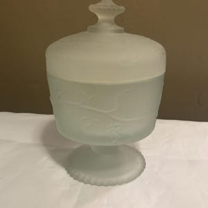 May include: A frosted glass candy dish with a lid. The dish has a floral design and a pedestal base.
