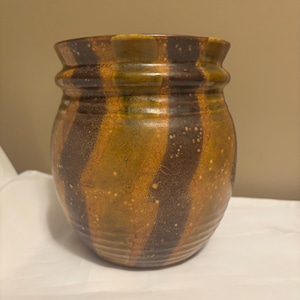 May include: A handcrafted ceramic vase with a rounded body and a ruffled rim. The vase features a warm color palette of brown and gold, with vertical stripes and speckled details. The pottery is suitable for home decor.