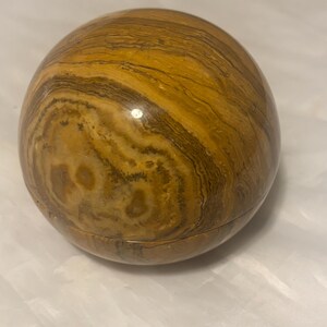 May include: A spherical, decorative object with a banded pattern in shades of brown and tan. The surface has a polished, glossy finish. The object appears to be made of stone or a similar material. The item is a decorative sphere.