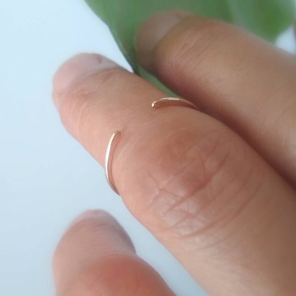 May include: A thin gold ring worn on a finger. The ring is open and has a simple design.