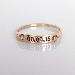 Op de afbeelding: Een gouden ring met een rechthoekige plaat gegraveerd met de datum "06.06.15".