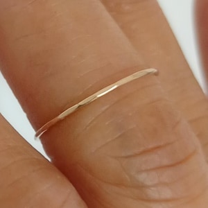 Puede incluir: Un delicado y fino anillo de oro se muestra en un dedo. El anillo tiene un diseño simple y minimalista, con una superficie lisa y ligeramente texturizada. Una pieza de joyería clásica.