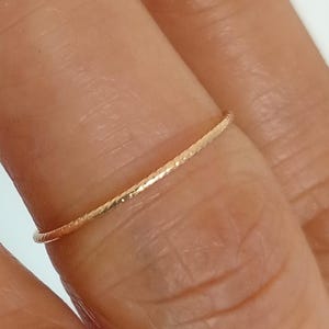 Puede incluir: Un delicado y fino anillo de oro con una superficie texturizada. El anillo se lleva en un dedo, mostrando su diseño simple pero elegante. El perfil delgado y la textura sutil del anillo crean una estética refinada.