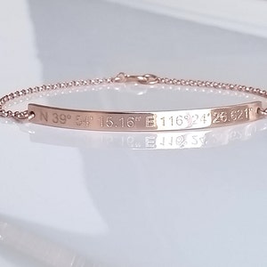 May include: A rose gold bracelet with a thin chain and a bar charm engraved with the coordinates "N 39° 54' 15.16" E 116° 24' 26.521".