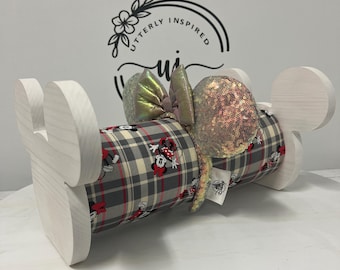 May include: A wooden display stand with a plaid fabric roll featuring Minnie Mouse. The stand has Mickey Mouse ear-shaped accents. A sequined bow and ears are attached to the fabric roll. The background has the text "Utterly Inspired".