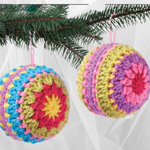 May include: Two colorful crocheted ornaments hanging from a Christmas tree branch. The ornaments are made with a variety of colors, including pink, purple, green, yellow, and blue. The ornaments are round and have a textured surface.