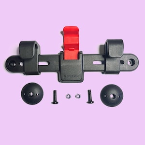 May include: A black bicycle accessory with a red lever and the text "KLICKfix". Includes two black mounting brackets, two black round pieces, two bolts, and two nuts. The components are arranged on a light purple background.
