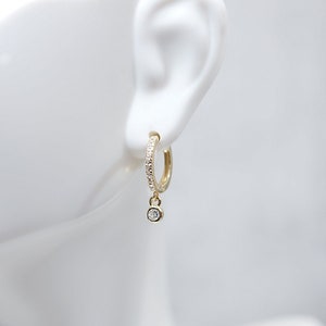 以下が含まれることがあります： 小さなダイヤモンドのチャームがついたゴールドのフープピアス。フープは小さなダイヤモンドが埋め込まれています。