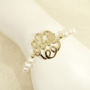 May include: A gold bracelet with a delicate, cursive "Love" charm and white pearl beads.