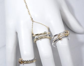 Könnte beinhalten: Ein Set aus drei Ringen in Gold und Silber, wobei zwei Ringe durch eine Kette verbunden sind. Die Ringe sind mit kleinen, klaren Steinen verziert.