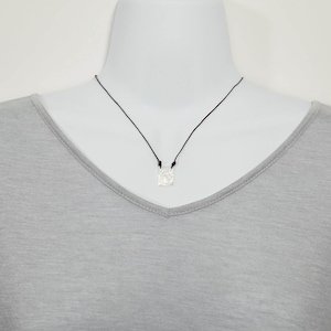 May include: A silver pendant necklace with a square-shaped pendant on a black cord.