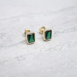 May include: A pair of gold earrings with emerald green rectangular gemstones.