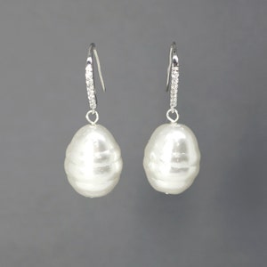 May include: A pair of silver earrings with a large white pearl drop and a row of clear cubic zirconia stones on the dangle.