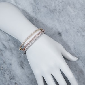Pode incluir: Três pulseiras de bracelete de ouro, prata e ouro rosa com uma fila de pedras de zircônia cúbica transparentes.