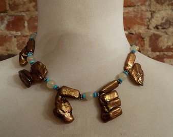 May include: A necklace made of iridescent brown and gold shell beads, white beads, and turquoise blue beads.