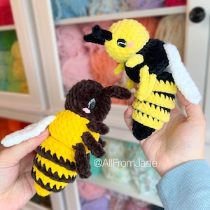 May include: Two crocheted bee plushies, one with black and yellow stripes and the other with brown and yellow stripes. Both have white wings and black eyes. The plushies are held in the hands of a person.