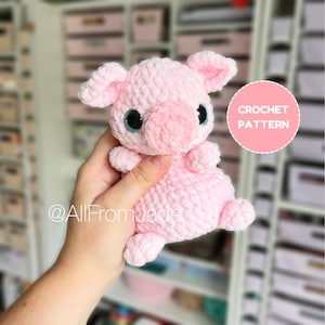 Könnte beinhalten: Ein handgehäkeltes rosa Ferkel mit großen, glitzernden blauen Augen und einer runden rosa Nase. Das Ferkel hat kleine Ohren und kurze Beine. Ein rosa Kreis mit den Worten "CROCHET PATTERN" befindet sich im Hintergrund.