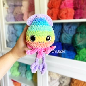 K&ouml;nnte beinhalten: Ein handgefertigter, pl&uuml;schiger, regenbogenfarbener Oktopus mit gro&szlig;en, reflektierenden Augen und einem l&auml;chelnden Gesicht. Der Oktopus hat ein weiches, strukturiertes Aussehen, mit einem Farbverlauf von Lila &uuml;ber Rosa, Gelb, Gr&uuml;n bis Blau. Die Tentakel sind in einem helleren Lilaton gehalten.