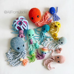 Peut inclure: Une collection de peluches poulpes en crochet de différentes couleurs, notamment bleu, vert, rose, jaune et orange. Les peluches ont des motifs et des textures différents, et certaines ont de petites perles pour les yeux. Les peluches sont disposées sur un fond blanc. @AllFromJade