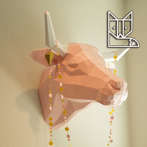 May include: A pink paper mache bull head with gold and pink paper circle garland hanging from its horns. The bull head is mounted on a wall.