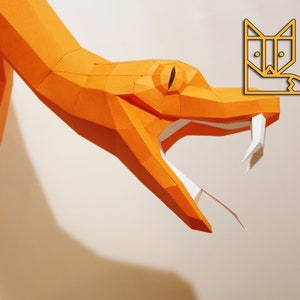 Könnte beinhalten: Nahaufnahme einer orangefarbenen Papierschlange mit offenem Maul, die weiße Zähne zeigt. Die Schlange ist aus gefaltetem Papier gefertigt und hat ein realistisches Aussehen.