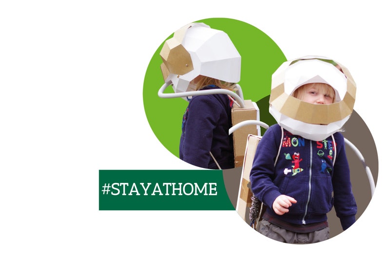 May include: Two children wearing cardboard astronaut helmets and backpacks. The child in the foreground is wearing a blue sweatshirt with a colorful graphic print. The text #STAYATHOME is displayed on a green rectangle.