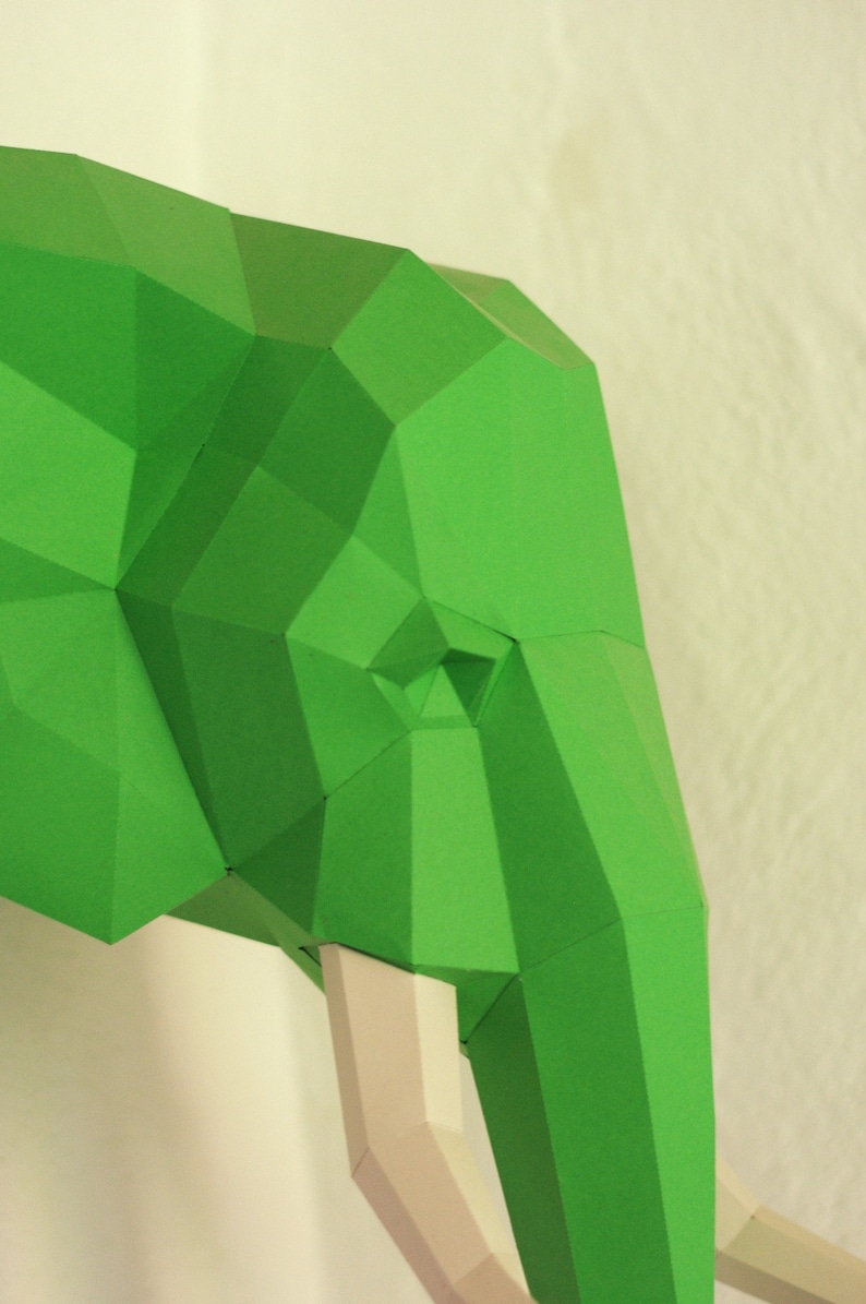 Pu&ograve; includere: Una testa di elefante di carta verde con zanne bianche. L'elefante &egrave; fatto di carta piegata e ha un design geometrico.