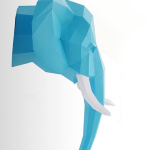 Pu&ograve; includere: Una scultura di testa di elefante in carta blu con zanne bianche. La scultura &egrave; realizzata in carta piegata e ha un design geometrico.