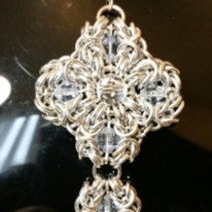 May include: A silver chainmail pendant with clear crystal beads. The pendant is in the shape of a cross with three smaller crosses hanging below it.