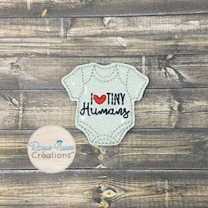 Op de afbeelding: Een lichtblauwe baby romper met een rood hart en de tekst "Ik hou van kleine mensen" geborduurd erop.