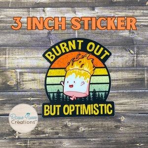 May include: A 3 inch sticker with a retro design featuring a cartoon marshmallow on fire with the text "Burnt Out But Optimistic".