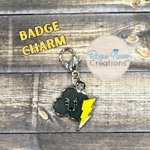 May include: A metal badge charm featuring a dark gray cloud with an angry facial expression and a bright yellow lightning bolt. The charm includes a silver-toned lobster clasp. Text in the image reads BADGE CHARM and Rogue Nurse Creations.
