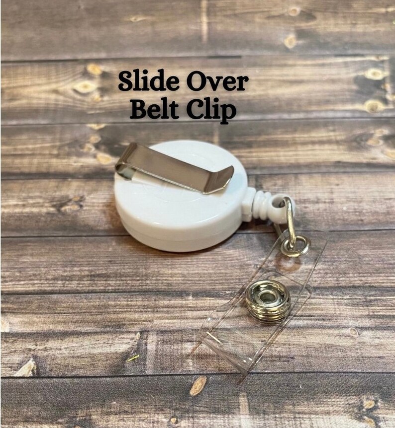 Op de afbeelding: Witte intrekbare badgehouder met een schuifbare riemclip. De houder heeft een transparante plastic band en een zilveren metalen knop.