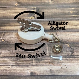 Op de afbeelding: Witte intrekbare badge-rol met een alligatorclip en een transparante plastic band. De rol heeft een 360 graden draaiing en de tekst "Alligator Swivel" en "360&deg; Swivel" staat op de afbeelding.