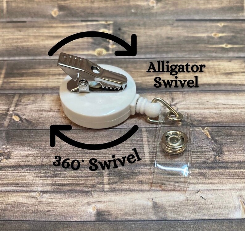 Op de afbeelding: Witte intrekbare badge-rol met een alligatorclip en een transparante plastic band. De rol heeft een 360 graden draaiing en de tekst "Alligator Swivel" en "360&deg; Swivel" staat op de afbeelding.