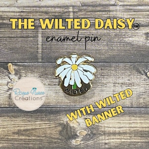 May include: A gold-colored enamel pin featuring a white and yellow daisy with the text "THE WILTED DAISY" and "enamel pin". The pin has a banner that says "WITH WILTED BANNER". The pin is on a wooden surface.