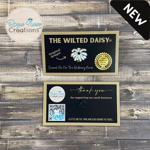May include: Two cards with gold trim. The top card has a black background with white text that reads "The Wilted Daisy" and "Enamel Pin For The Ordinary Nurse". A white daisy enamel pin is on the card. The bottom card has a black background with white text that reads "Rogue Nurse Creations" and "thank you for supporting my small business". A black and white QR code is on the card. The text "A little wilted, torn, and dead around the edges..." is on the card. The word "NEW" is in a white box with a black outline.