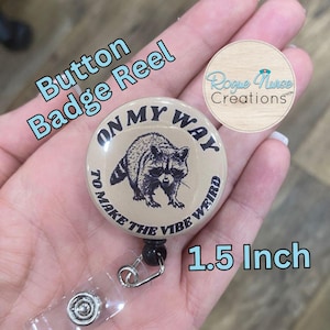 May include: A 1.5 inch button badge reel with a tan background and a black and white raccoon graphic. The text on the badge reads "On My Way To Make The Vibe Weird".