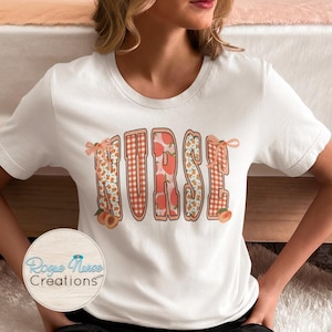 May include: White t-shirt with the word "NURSE" in a peach and floral design. The letters are outlined in a peach gingham pattern, with peach and floral patterns inside. Small peach illustrations and bows accent the design. The Rogue Nurse Creations logo is visible.