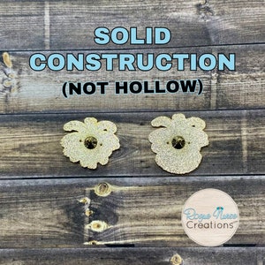 May include: Two gold-coloured enamel pins with glitter detail. The pins are shaped like a flower with a single rhinestone in the centre. The text "SOLID CONSTRUCTION (NOT HOLLOW)" is displayed above the pins. The text "Rogue Nurse Creations" is displayed below the pins.