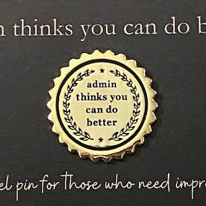 May include: Gold-colored pin with a laurel wreath design and the text "admin thinks you can do better".
