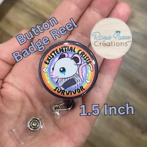 May include: A 1.5 inch button badge reel with a black background and a colorful rainbow design. The badge features a cartoon possum with a tear on its cheek and the text "Existential Crisis Survivor".
