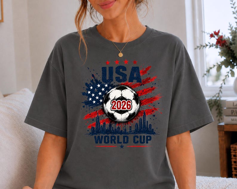 USA Soccer World Cup 2026 graphic shirt featuring soccer ball, American flag splash art, skyline design and patriotic football fan aesthetic