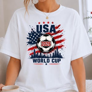 USA Soccer World Cup 2026 graphic shirt featuring soccer ball, American flag splash art, skyline design and patriotic football fan aesthetic